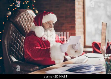 Profil côté photo excité cheveux gris santa claus s'asseoir table impressionné obtenir liste de souhaits lettre x-mas miracle foire noël noël noël casquette rouge celebration wear Banque D'Images