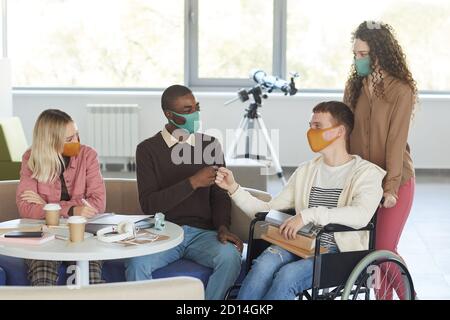 Portrait d'un groupe multiethnique d'étudiants portant des masques tout en étudiant dans la bibliothèque d'université avec un jeune homme utilisant un fauteuil roulant en premier plan, espace de copie Banque D'Images