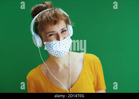 La vie durant la pandémie du coronavirus. Portrait d'une femme étudiante moderne souriante en chemise jaune avec masque médical écoutant de la musique avec un casque Banque D'Images