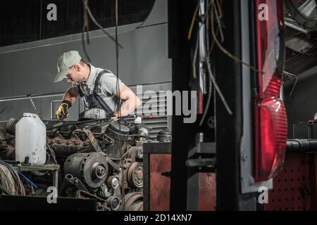 Technicien automobile caucasien dans ses années 40 réparation et restauration du vieux moteur diesel de camion lourd. Travailleur en atelier de l'industrie automobile. Banque D'Images