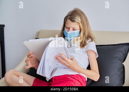 Enfant fille dans le masque de visage assis sur le canapé avec l'école ordinateur portable Banque D'Images