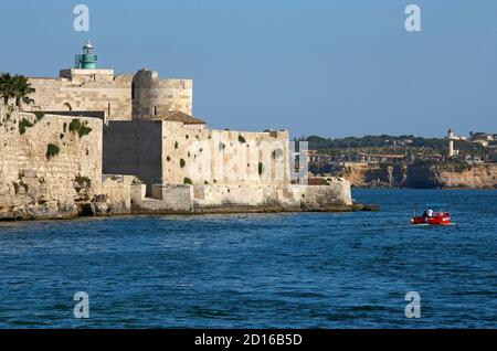 Italie, Sicile, Syracuse, île d'Ortigia, petit bateau de pêche passant devant le fort de castello Maniace face à la mer Banque D'Images