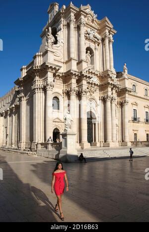 Italie, Sicile, Syracuse, île d'Ortigia, élégante fille italienne en robe rouge passant devant la cathédrale de Syracuse sur la place du duomo Banque D'Images