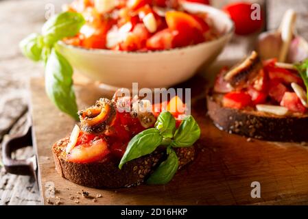 Savoureux hors-d'œuvre italiens savoureux bruschetta, tranches de pain garni de basilic tomate, gros plan sur un panneau de bois Banque D'Images