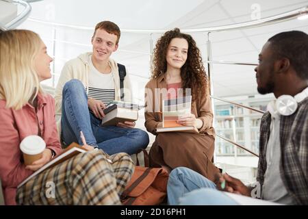 Groupe multiethnique d'étudiants assis sur les escaliers dans l'université et discuter tout en travaillant sur les devoirs Banque D'Images