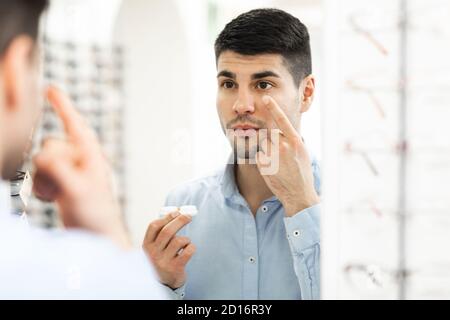 Un gars tenant un contenant appliquant des lentilles de contact pour les yeux Banque D'Images