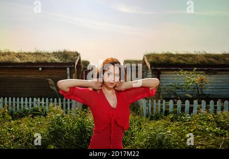 la fille dans la robe rouge debout sur l'arrière-plan de maisons en bois Banque D'Images