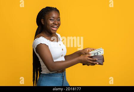 Finance, investissement et économies d'argent. Bonne femme noire mettant des billets dans un portefeuille Banque D'Images