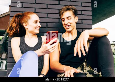 une jeune femme parle à un jeune homme et montre son smartphone après avoir fait de l'exercice à la salle de gym Banque D'Images