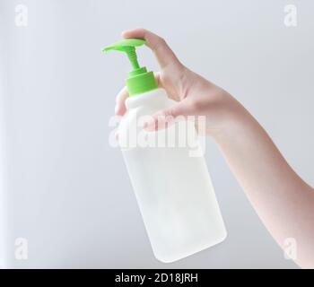La main de la jeune femme tenant le détergent en bouteille sanitaizer blanc pour différentes surfaces dans la cuisine, la salle de bains et d'autres pièces. Gros plan. Fond gris clair. Concept de nettoyage de la salle de bain Banque D'Images