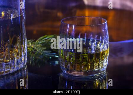 Carafe et verre avec whisky et brindilles de pin sur un fond flamboyant. La carafe et le verre sont mis en miroir sur une table en verre. Banque D'Images