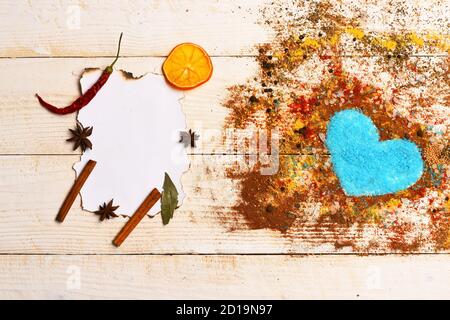 Concept art de l'alimentation. Ensemble d'épices sur fond de bois beige. Composition de ce condiment forme de coeur rempli de sel bleu. Morceau de papier avec des bâtons de cannelle, d'anis étoile et sécher les tranches d'orange. Banque D'Images