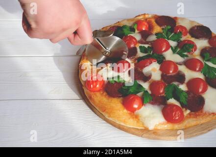 main humaine avec pizza coupée dans la cuisine. pizza italienne maison. pepperoni traditionnel avec tomates, mozzarella et salami. Banque D'Images