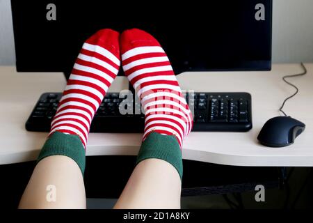 Jambes de femmes en chaussettes de Noël sur le bureau avec PC et clavier. Concept de célébration du nouvel an, costume d'orf Banque D'Images