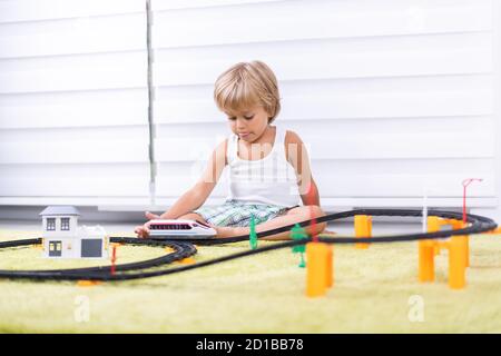 Un petit garçon joue avec un chemin de fer en plastique. Enfant avec train jouet. Jouets éducatifs pour les jeunes enfants. Petit garçon construisant des voies de chemin de fer sur un tapis vert. Banque D'Images