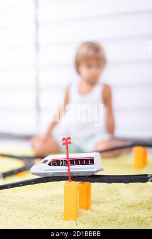 Un petit garçon joue avec un chemin de fer en plastique. Enfant avec train jouet. Jouets éducatifs pour les jeunes enfants. Petit garçon construisant des voies de chemin de fer sur un tapis vert. Banque D'Images