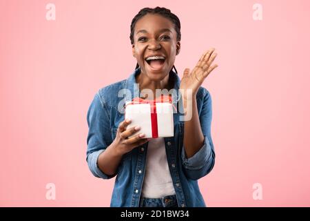 Joyeuse femme noire criant tenant cadeau d'anniversaire sur fond rose Banque D'Images