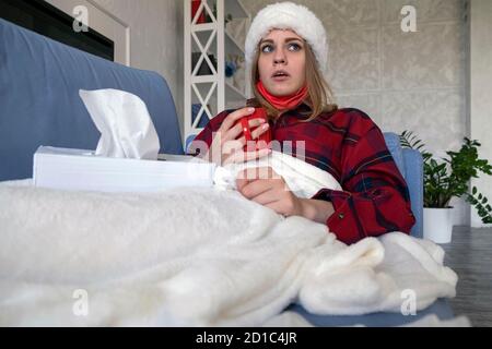Concept santé, froid, vacances et personnes. Malade jeune femme caucasienne couché sur un canapé et buvant du thé chaud de la tasse rouge portant le chapeau de santa à la maison Banque D'Images