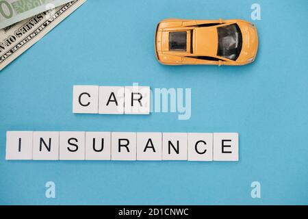 Blocs en bois avec des mots assurance de voiture. Entreprise de location, propriété. Concept de protection et de sécurité. Voiture jouet jaune et billets sur fond bleu tendance Banque D'Images