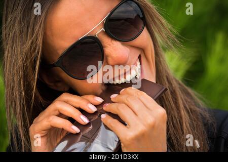 Jolie jeune femme fatiguée de stress et très heureuse de manger une barre de chocolat noir. Mordre le chocolat noir au coucher du soleil Banque D'Images