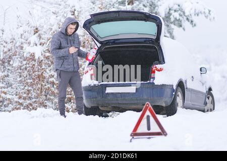 Homme tenant une bouteille d'antigel froid devant les bagages de la voiture endommagée. Banque D'Images