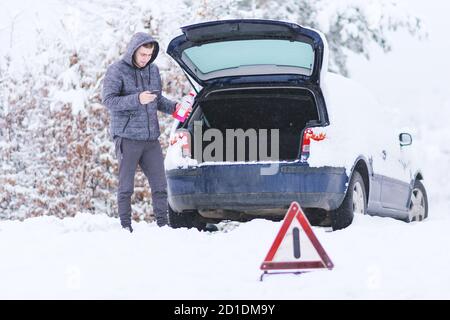 Homme tenant une bouteille d'antigel froid devant les bagages de la voiture endommagée. Banque D'Images