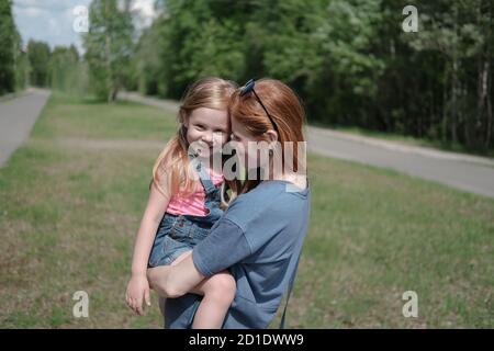 la mère et la fille s'embrassent à l'extérieur. la famille aux cheveux de gingembre. la femme aux cheveux rouges tient sa petite fille et souriante. concept de famille heureux. Banque D'Images