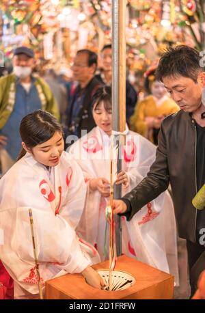 asakusa, japon - novembre 08 2019 : jeune fille japonaise Miko dans un kimono religieux traditionnel shōzoku faisant une loterie avec un diable tuant la flèche hamaya à S. Banque D'Images