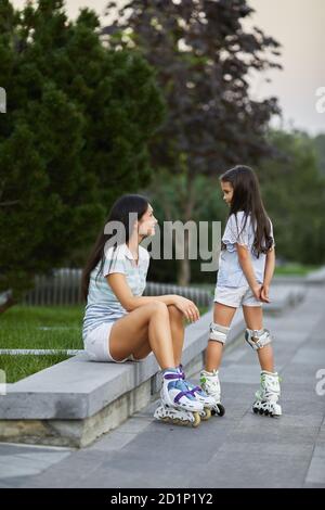 une petite fille heureuse et sa mère portent des patins à roulettes tout en étant assise dans le parc d'été. Banque D'Images