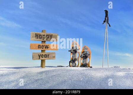 panneau en bois avec texte bonne année dans la neige à côté des raquettes et des bâtons de ski Banque D'Images