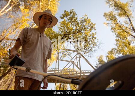 L'homme dans un chapeau de cow-boy utilise un détecteur de métal pour recherchez les trésors enfouis en automne avec le changement feuillage vu d'un angle bas Banque D'Images