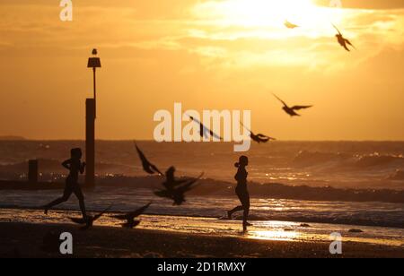 Deux nageurs s'encourent dans la mer tandis que le soleil se lève sur la plage de Boscombe à Dorset. Banque D'Images