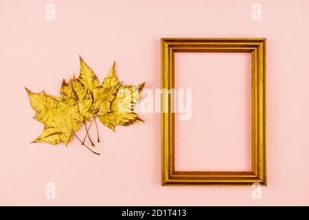 f feuilles d'érable dorées et cadre photo en bois sur fond rose. Concept tendance. Pose en flanelle dans un style minimaliste Banque D'Images