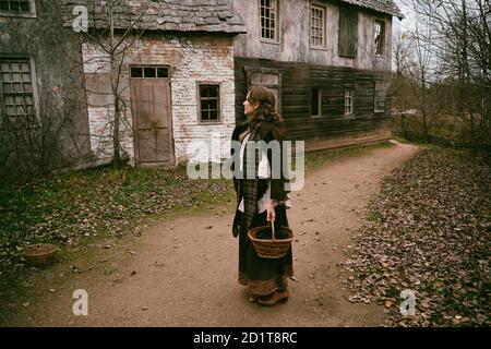 Jeune femme en robe vintage avec panier en osier sur le vieille rue d'une ville médiévale Banque D'Images