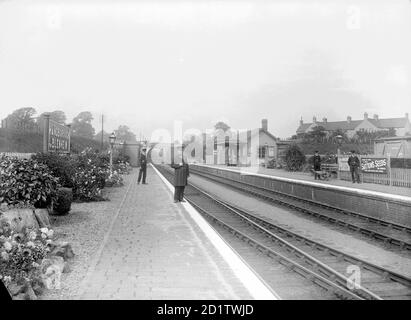 LONGUE gare de HANBOROUGH, West Oxfordshire. Le Maître de la gare et un garde debout sur la plate-forme de la petite gare, avec un pont de chemin de fer visible en arrière-plan. Un porteur avec un chariot se trouve sur la plate-forme opposée. Photographié par Henry Taunt en 1920. Banque D'Images