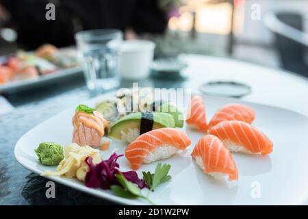 Une assiette de sushis sur une table à l'extérieur dans un restaurant. L'assiette contient des sushis nigiri au saumon, des sushis nigiri à l'avocat et des petits pains californiens. Une alimentation saine Banque D'Images