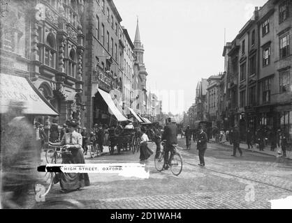 High Street, Oxford, Oxfordshire. Vue extérieure donnant sur la rue animée de Carfax avec des chariots à cheval, des tramways et des vélos dans la rue. Banque D'Images