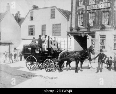 High Street, Burford, West Oxfordshire, Oxfordshire. Un bus tiré par des chevaux et des passagers attendent dans la rue devant l'hôtel, à l'origine du XVIe siècle, mais avec une façade du XVIIIe siècle, sous la surveillance d'enfants locaux. Banque D'Images