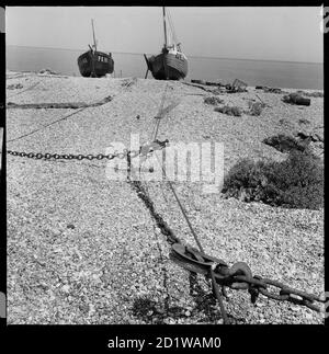 Dungeness, Lydd, Shepway, Kent. Une vue sur la plage vers une paire de bateaux de pêche avec un treuil au premier plan. Banque D'Images