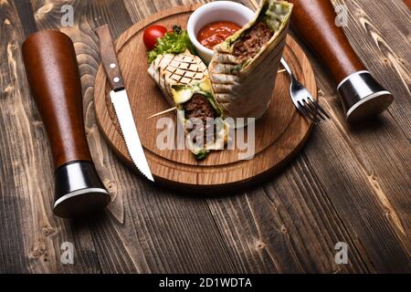 Concept de plat principal. Viande hachée enveloppée de pain de lave-glace sur fond de bois. Burrito ou tortilla servi dans le restaurant ou le café. Pain plat avec garniture de porc ou de poulet et sauce Chili rouge. Banque D'Images