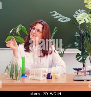 REDHEAD enseignante de biologie féminine dans une leçon à l'école. Femme scientifique avec plante verte en main Banque D'Images