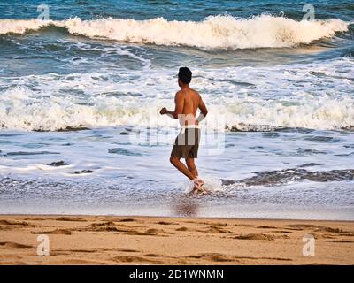 PUDUCHERRY, INDE - DÉCEMBRE CIRCA, 2018. Silhouette masculine non identifiée dans l'eau de mer sur une plage de sable. Jeune garçon adulte sur la plage - magnifique dos Banque D'Images