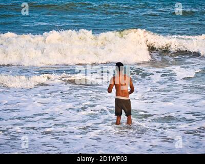 PUDUCHERRY, INDE - DÉCEMBRE CIRCA, 2018. Silhouette masculine non identifiée dans l'eau de mer sur une plage de sable. Jeune garçon adulte sur la plage - magnifique dos Banque D'Images