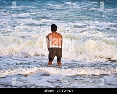 PUDUCHERRY, INDE - DÉCEMBRE CIRCA, 2018. Silhouette masculine non identifiée dans l'eau de mer sur une plage de sable. Jeune garçon adulte sur la plage - magnifique dos Banque D'Images