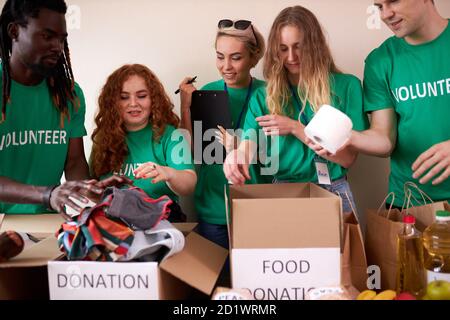 jeunes volontaires enthousiastes avec des dons pour les pauvres, boîte en carton avec des vêtements pour la charité. les gens gentils aident les pauvres, des étuis pleins de vêtements pour les pauvres dons, concept d'activité sociale Banque D'Images