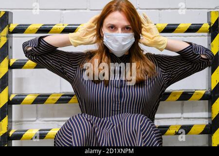 Une jeune femme dans un masque médical et des gants sur le fond de la barrière restrictive, concept. Quarantaine et isolement des personnes pendant le coronavirus. Banque D'Images