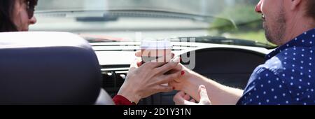 Homme et femme s'assoient en voiture et tiennent un verre de boisson ensemble Banque D'Images