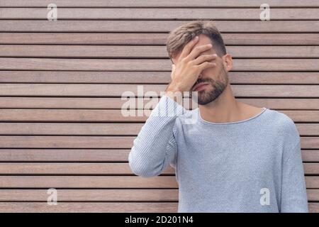 Facepalm. Honte embarrassé homme couvrant son visage. Jeune homme sur fond de mur en bois avec espace de copie. Émotion expression faciale et sentiments conce Banque D'Images