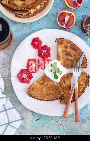 Crêpes fines avec sauce à la crème aigre, garniture au chocolat, menthe et pamplemousse sur une assiette bleue avec une serviette blanche Banque D'Images