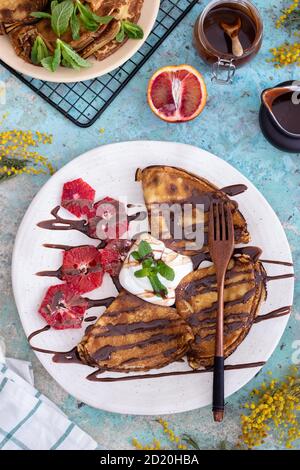 Crêpes fines avec sauce à la crème aigre, garniture au chocolat, menthe et pamplemousse sur une assiette bleue avec une serviette blanche Banque D'Images
